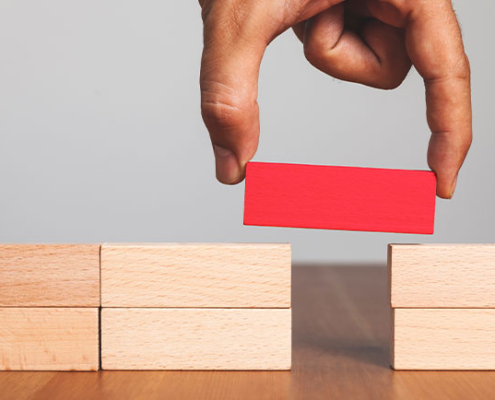 Close-up of a hand placing a red block to bridge a gap between two stacks of wooden blocks—symbolizing problem-solving and reliable connection through managed IT support services Dallas.