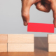 Close-up of a hand placing a red block to bridge a gap between two stacks of wooden blocks—symbolizing problem-solving and reliable connection through managed IT support services Dallas.